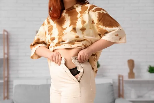 Image of woman trying to do her trousers up after pregnancy weight gain Havering