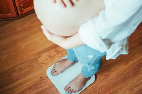 Image of woman weighing herself and experiencing weight gain through pregnancy Havering